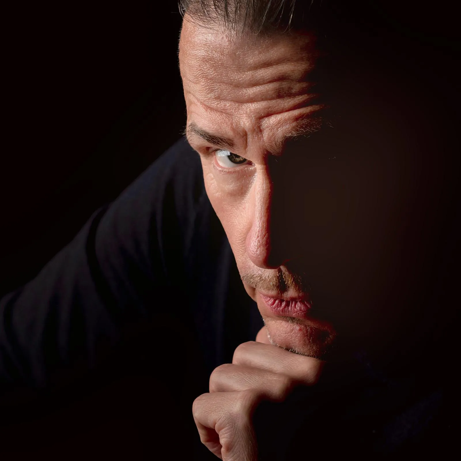 Half-lit portrait of Milan Vodrážka in shadow, hand resting at chin