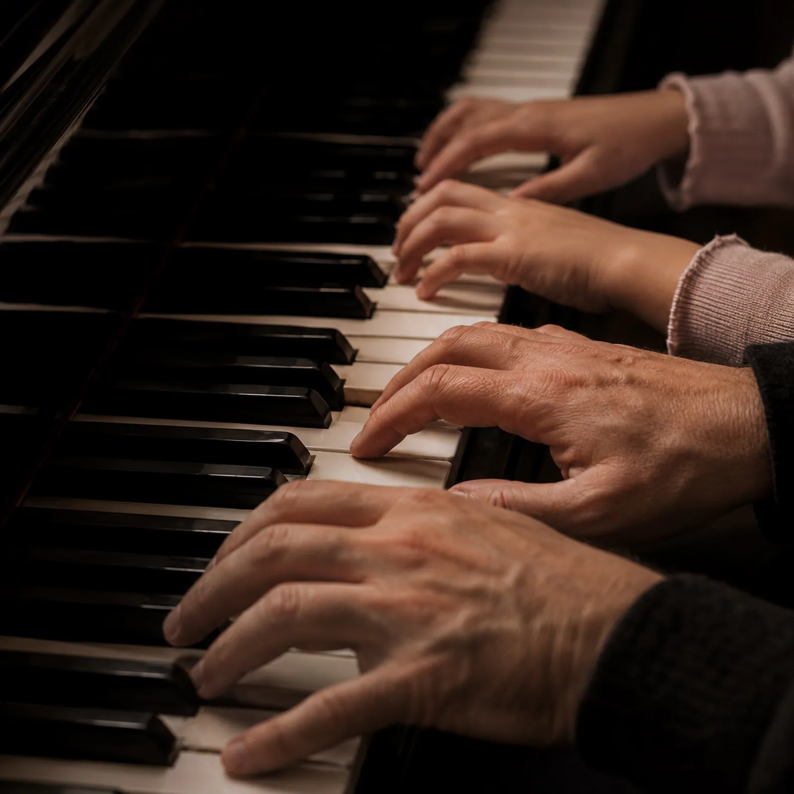 Close-up of an adult's and a child's hands playing piano together